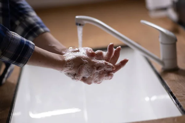 Washing hands with soap and water under the tap. Hygiene concept detail. Beautiful hand and a stream of water in the bathroom.