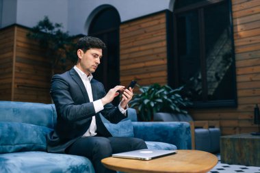 Ciddi bir iş adamı kanepeye oturur ve telefona bakar, haberlere bakar..