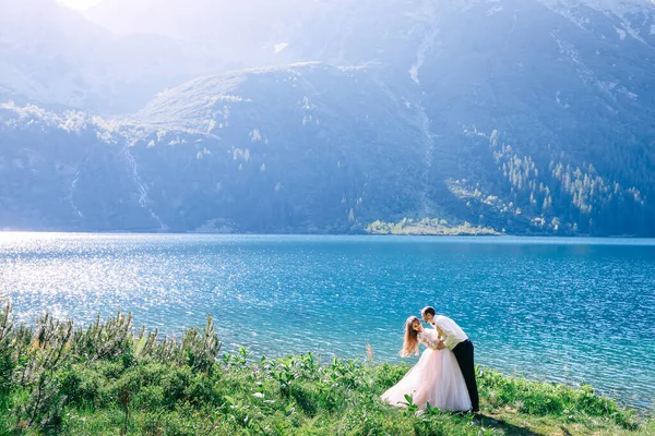 婚纱照会上 一对年轻夫妇在一座美丽的大湖畔的山上坠入爱河 夫妻们都在开心地微笑着 男人想吻新娘 — 图库照片