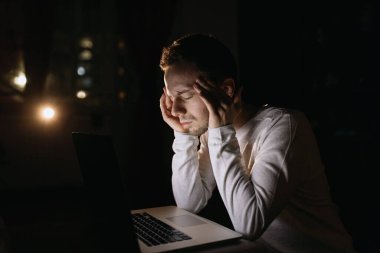 Bilgisayarda çalışan ve baş ağrısı çeken genç bir adam. Geceleri hasta ve yorgun hissediyorum.