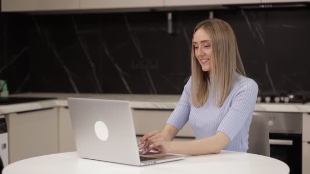 若い女性のフリーランサーはキッチンでノートパソコンを使って笑ったり — ストック動画
