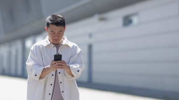 Ung Asiatisk Kjekk Mann Smiler Mens Han Leser Beskjeder Smarttelefon – stockvideo