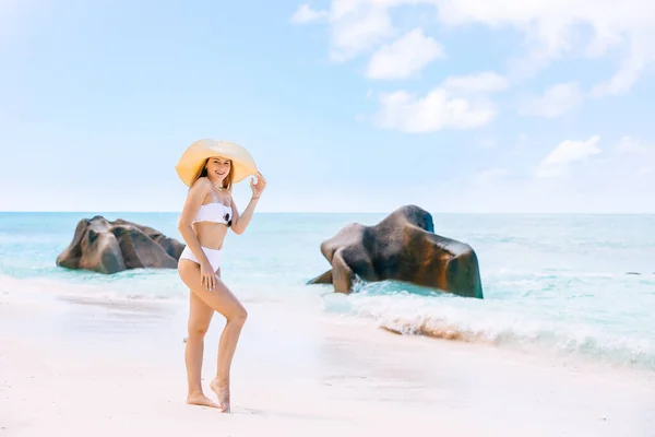 白いビキニとビーチハットを身に着けている若い女性は セーシェルのLa Digue島で素晴らしい景色のビーチを楽しんでいます 完璧な熱帯のビーチのコンセプトで夏の休暇 スペースのコピー — ストック写真