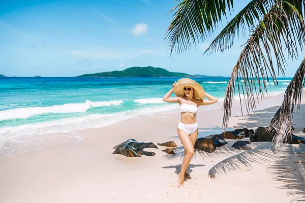 エキゾチックなビーチで若い女性を気をつけてください 美しい水着の女の子と大きな帽子が海を背景にビーチに沿って歩いています — ストック写真