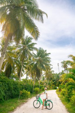 Happiness woman traveler with her bicycle rides trail between palm trees in sunny summer day on beach. Freedom, Travel, Journey, concept.