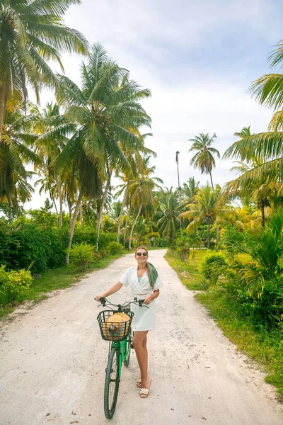 An elegant happy woman in a white dress rides a bicycle around La Digue island in the Seychelles. Happy lifestyle on summer tropical vacation