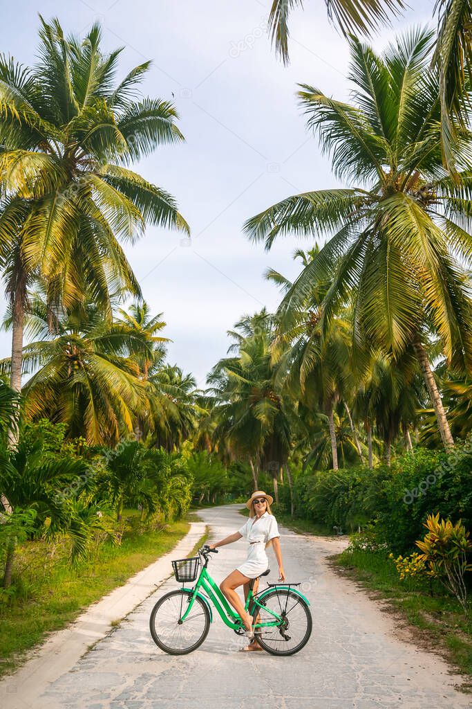 Girl is cycling on her old vintage bicycle through the jungle of Anse Source dArgent, la Digue, Seychelles. She is surrounded by palm trees and flowers. Enjoying her beautiful holiday. 