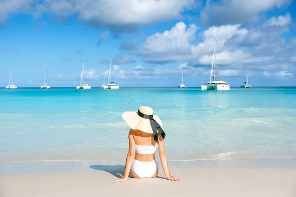 在大海 蓝天和游艇的背景下 一个身穿泳衣 头戴草帽的年轻女子坐在热带海滩上的后视镜 — 图库照片