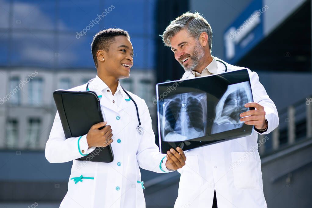 Medical workers outside the hospital are talking about x-rays. Physicians consult with each other. Two doctors look at an MRI and discuss it.
