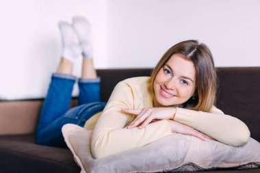 Boş zamanlarında evdeki kanepede uzanan genç bir kadın. Mutlu kız, aydınlık bir kış sabahı evinde dinleniyor..