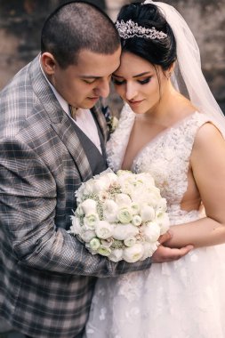 Yeni evliler birbirlerine yaslanırlar ve şık bir düğün buketine bakarlar. Beyaz güllerden ve şakayıklardan oluşan bir buket.