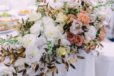 Masada yeni evliler için bir buket orkide, gül ve şakayık var. Buket altın dallarla tamamlanır..