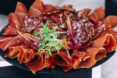 Aperatif jambonlu siyah tabak ve roka yapraklarıyla süslenmiş salam. düğün resepsiyonu.