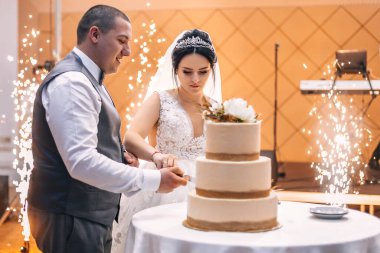 Yeni evliler üç katlı bir pasta kestiler. Restoran salonunda havai fişekler. düğün günü.