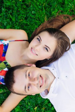 Parktaki çimlerin üzerinde yatan romantik iki genç insan. Birbirlerinin omuzlarında yatarlar ve birbirlerine sarılıp gülümserler. Mutlu görünüyorlar. Yukarıdan görüntüle.
