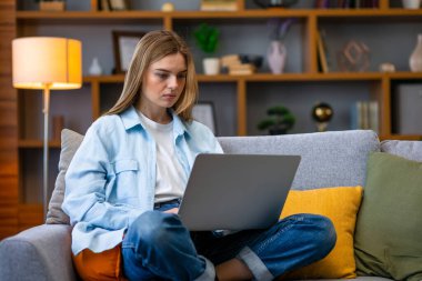 Ciddi bir kadın kanepeye oturmuş online alışveriş sitesine göz gezdiriyordu. Evde boş zamanlarında internette gezinen mutlu kız..