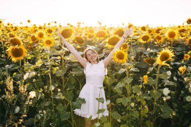 Güzel genç dişi gün batımında ayçiçeği tarlasında doğanın tadını çıkarıyor.