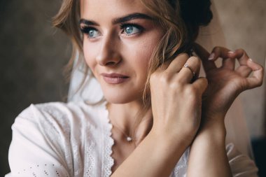 Hoş bir gülümsemesi ve güzel gözleri olan zarif bir gelin küpe takar. Gelin sabahı.