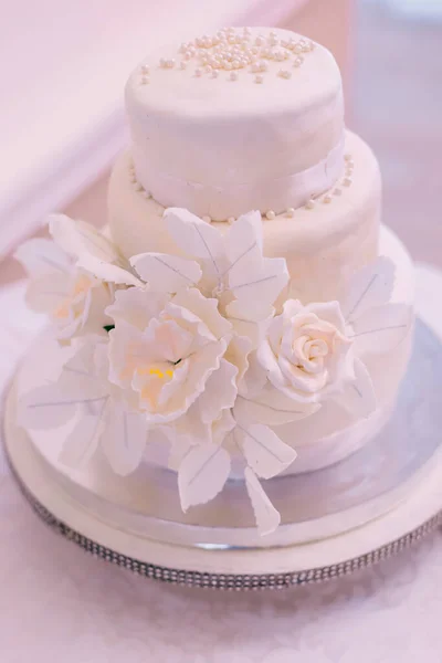 white wedding cake decorated with mastic flowers on a white table.