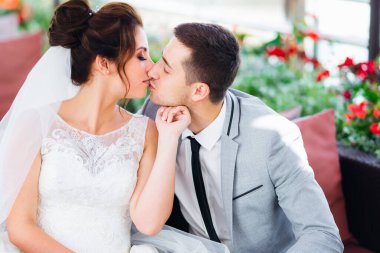 Yeni evliler restorandaki kanepede öpüşür ve oturur.