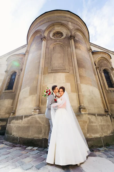 Vőlegény Átfogja Megcsókolja Menyasszonyt Háttérben Egy Régi Épületet Gyönyörű Építészet — Stock Fotó