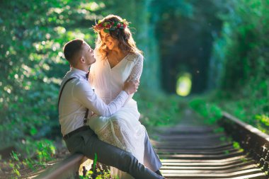 Çift oturan ve demiryolu sarılmak. ağaç tüneli. şenlikli giyim