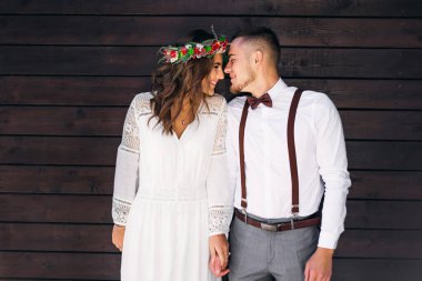 couple near the wooden wall hold hands, closed their eyes and smile. couple in festive clothes. girl with a wreath on the head