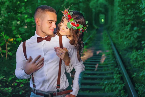 彼女の頭の上に花輪を持つ女の子はひげを持つ男を抱擁します 鉄道線路と樹木のトンネル — ストック写真