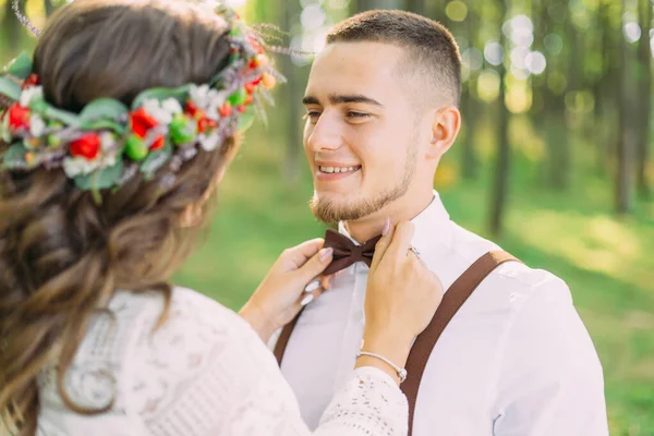 guy smile in a white shirt with bow tie and suspenders. the girl in a wreath fixes a bow tie. close up