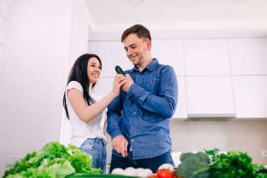 Young happy couple are enjoying and preparing healthy food in their kitchen.