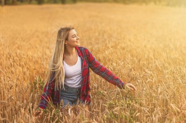 Girl in a red shirt on a background of a field with ripe wheat. Model posing on a warm summer morning. Copy space