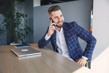 businessman in a suit with a laptop computer in the office talking on a mobile phone, deciding business issues, negotiating a deal.
