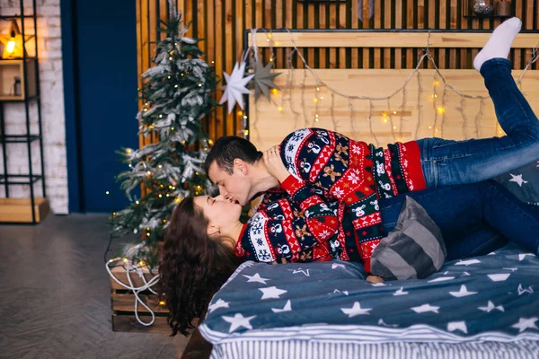 Erkek ve kız yatağa uzanır ve Noel ağacı arka planında gülümserler. profil.