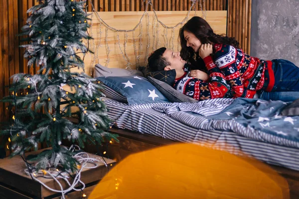 Adam ve kız yataktalar ve birbirlerine nazikçe bakıyorlar. Komodinin üzerinde çelenkler olan küçük bir Noel ağacı. Mercek parlaması.