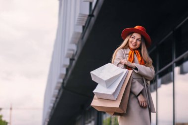 woman shopaholic with paper bags for shopping walks near modern building