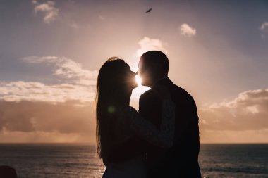 silhouettes of kissing newlyweds on sunset and ocean background. close up.