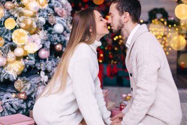 Gözleri kapalı bir kız ve erkek çocuğu profili var ve el ele tutuşuyorlar. Yılbaşı ağacı ve çelenk arka planında bir çift.