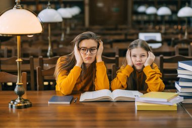 Sıkıcı ödev konsepti. Yorgun bir öğrenci ve liseli kız halk kütüphanesinde bir sürü kitapla bir masada oturuyorlar..