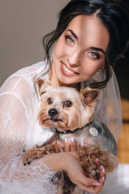 Kollarında Yorkshire teriyeri tutan ve gülümseyen güzel bir esmer gelin. Gelinin sabahki konsepti
