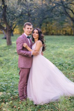 Gelin ve damat parkta çimenlikte. Kutlama gününde düğün yürüyüşü.