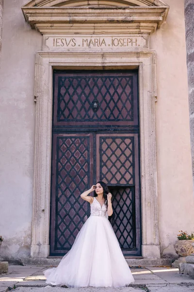 a bride with long black hair and a long dress stands by the black iron door at the entrance to the building.