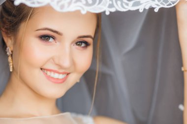 Gelin yüzünü bir duvakla örttü ve kameraya baktı. Güzel makyaj ve gülümseme.