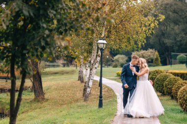 Yeni evliler parktaki ara sokakta yürüyorlar. Gelin ve damadın yürüyüşü mutlu bir çiftin düğün gününde.