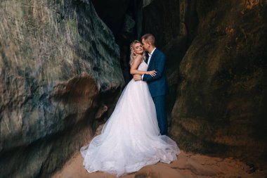 Güzel bir romantik düğün fotoğrafı. Damat gelinliği giymiş gelini öpüyor. Büyük kayaların yanında..