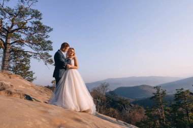 Mavi gökyüzünün arka planında yeni evliler. Adam elini gelinin omzuna koyar..