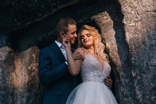 晴れた日に山の大きな岩の近くに抱擁豪華なウェディングドレスで花嫁と新郎のロマンチックな結婚式のカップルの美しいショット — ストック写真