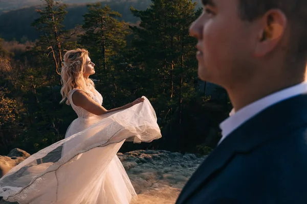 新娘站在山上的岩石上 手拿着白色的连衣裙旋转着 男人把目光移开了 — 图库照片