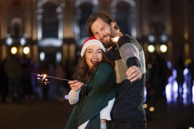 Have fun together on New Year's Eve. Two lovers hug and kiss holding sparklers.