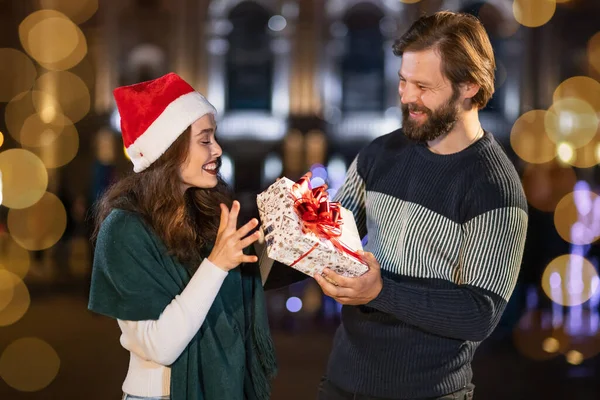 the guy gives the girl a gift on New Year\'s Eve on the street. The woman is delighted happy with the gift