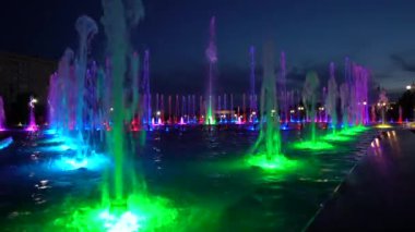 Büyük bir çeşmedeki birçok su püskürtüsü gece boyunca farklı renklerde parıldar.
